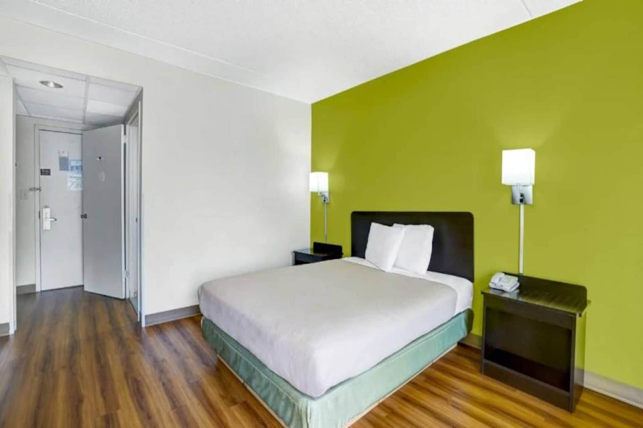 A hotel room with a bed, bedside tables, a door, and a green wall.