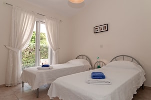 Una habitación con dos camas individuales, una ventana con cortinas, un cuadro colgado en la pared y una mesita de noche con lámpara.