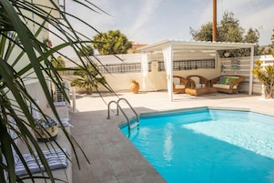 Una piscina con un área de estar cubierta, un deck de concreto y plantas en macetas.