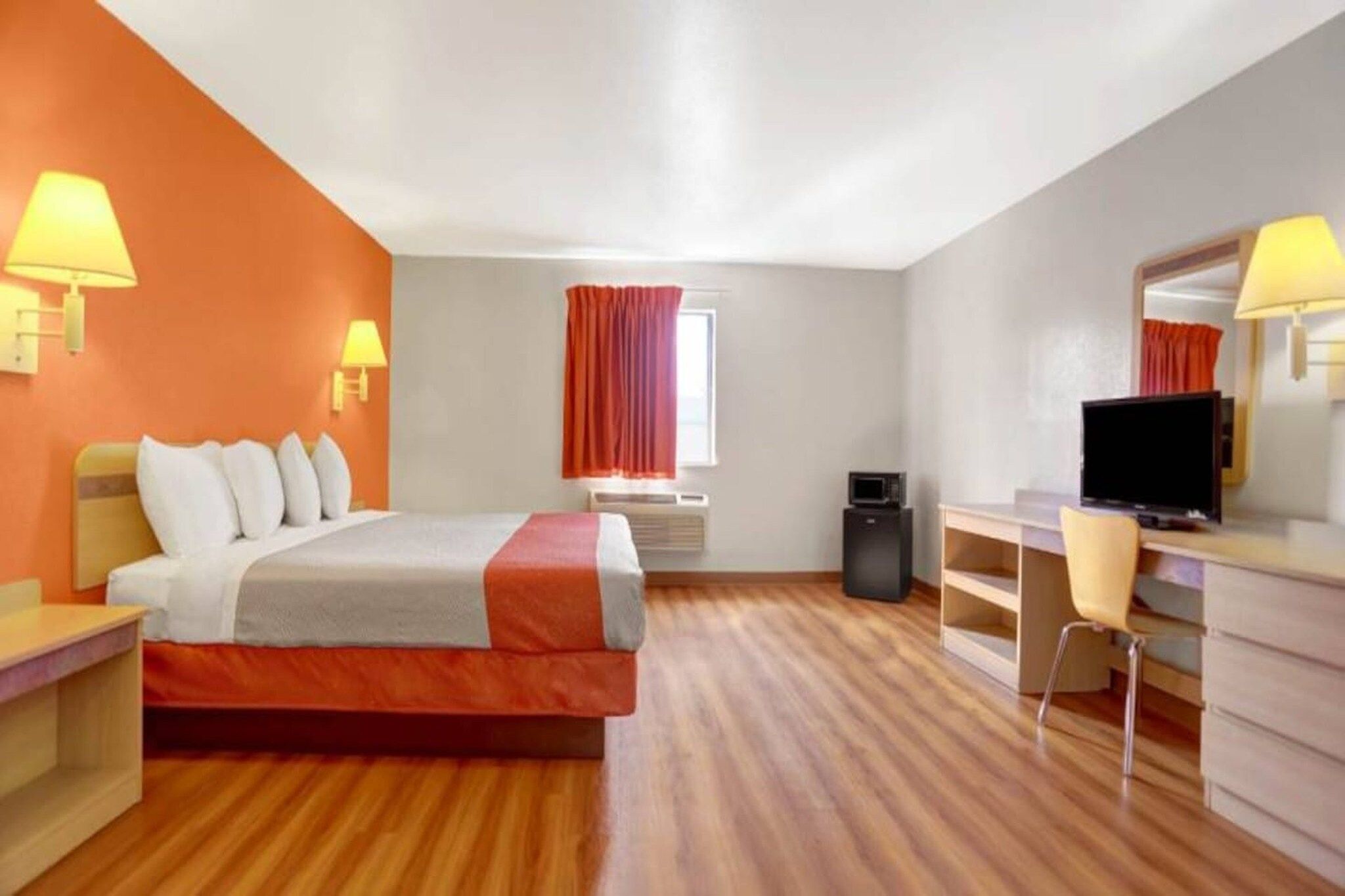 A hotel room with a bed, desk, chair, television, and a window with curtains.