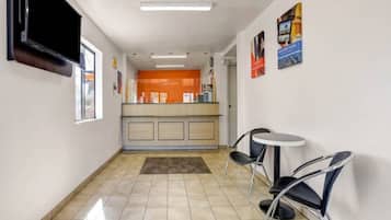 A hotel corridor with a reception desk, a small seating area with two chairs, and a tiled floor.