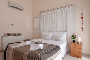 Habitación de hotel con cama, mesita de noche, aire acondicionado, radiador y una lámpara fijada a la pared.