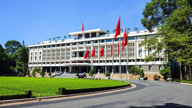Un grand bâtiment moderne, orné de plusieurs drapeaux rouges, avec une pelouse bien entretenue et une allée incurvée menant à l’entrée.