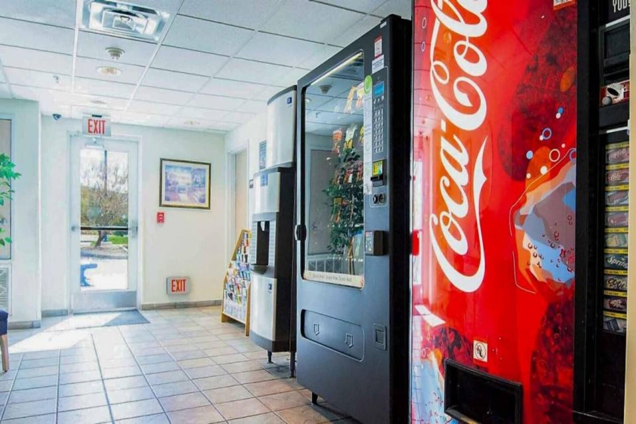 Automaatti, jossa on Coca-Colan logo, uloskäyntikyltti ja ovi, joka johtaa laatoitetulle käytävälle.