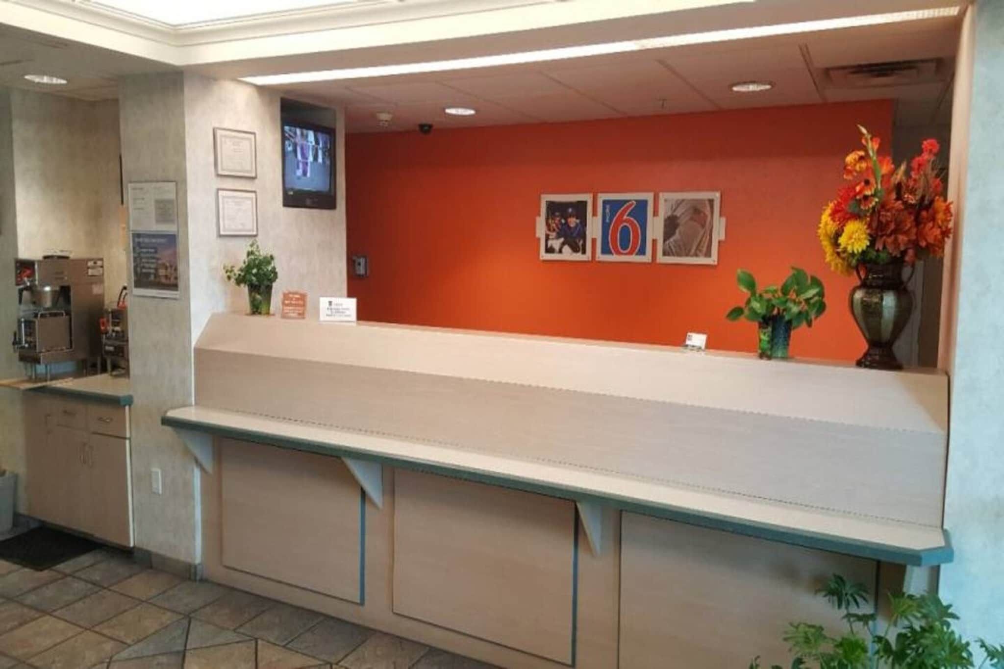 Un espace d’accueil avec un comptoir, une machine à café, des tableaux encadrés au mur et un vase de fleurs.