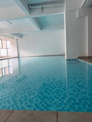En stor inomhuspool med ett rutmönstrat kakelgolv.