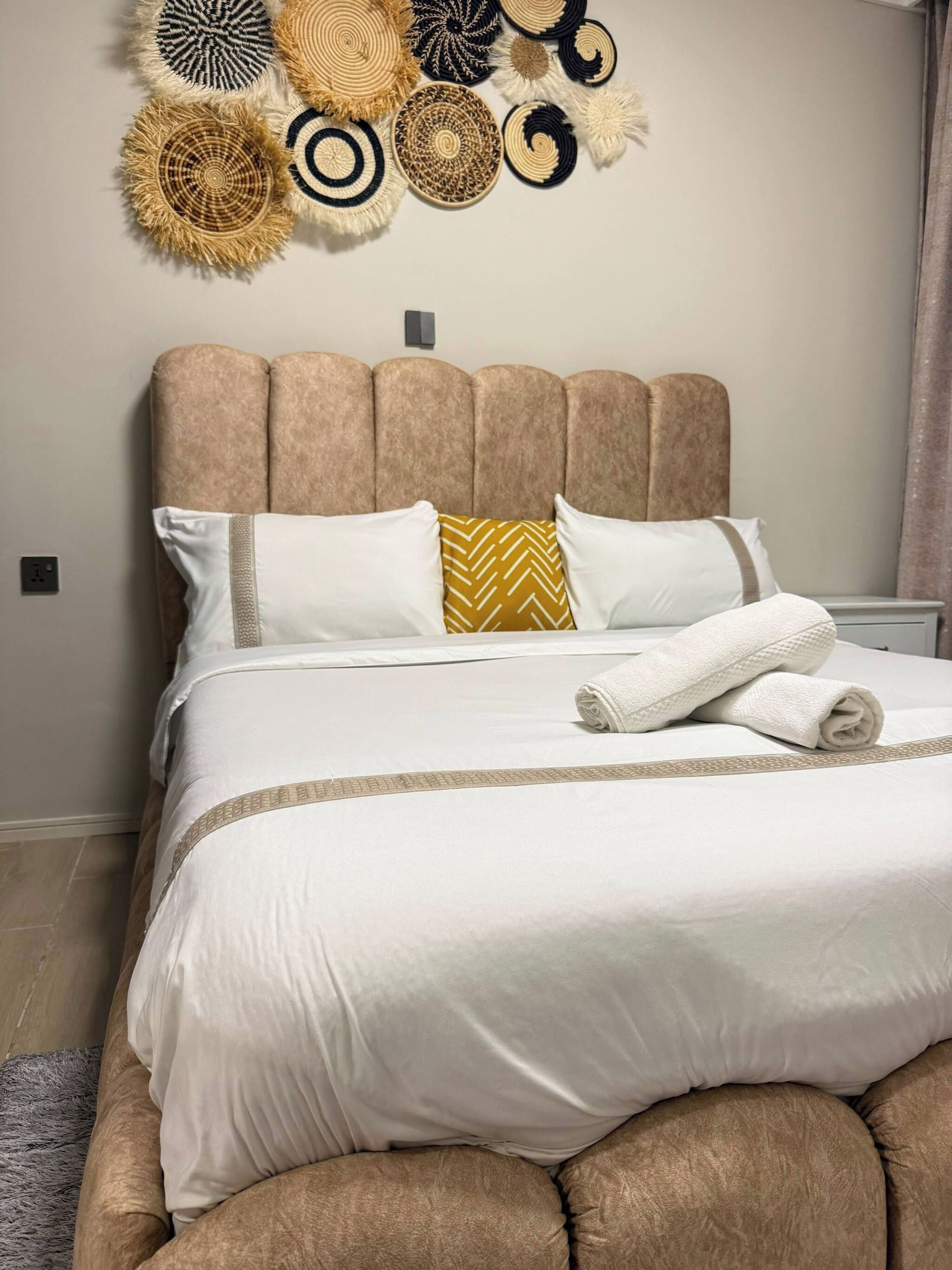 A neatly made bed with a headboard, pillows, and a rolled towel.