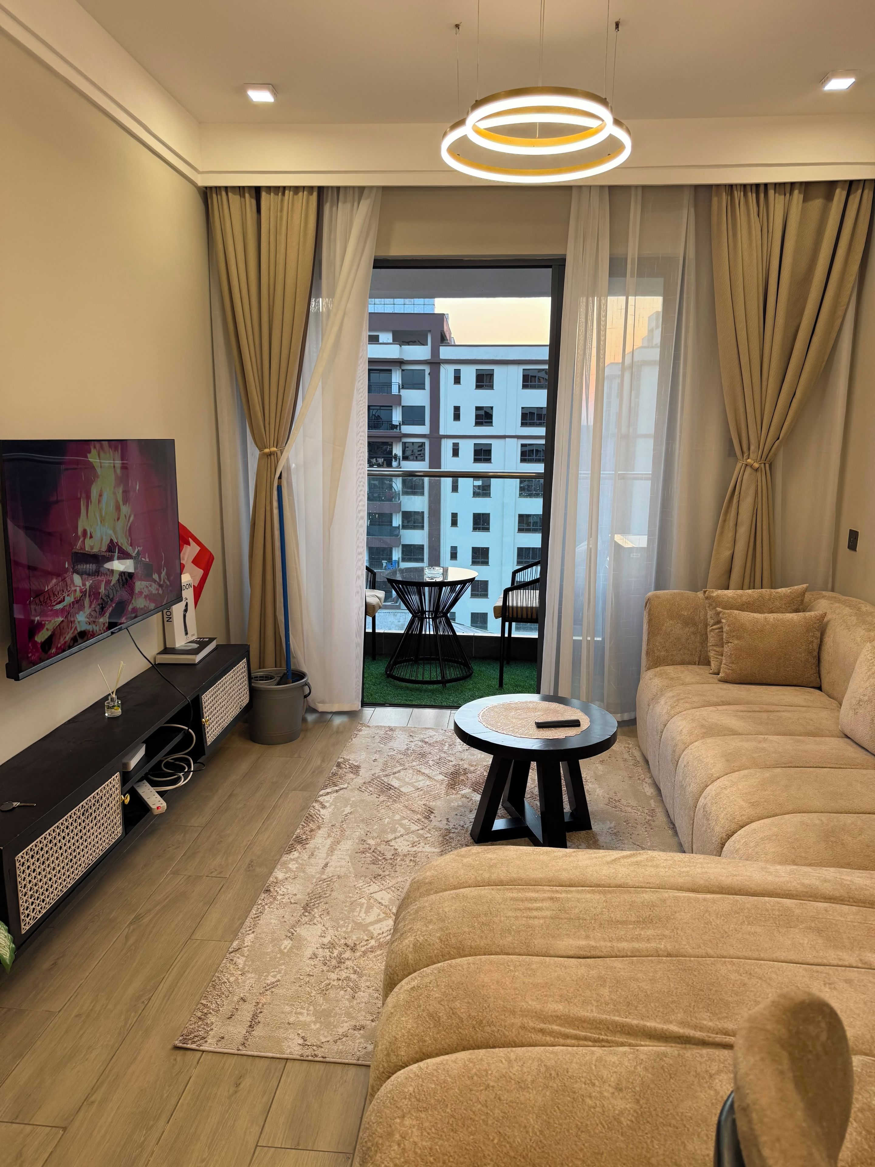 Un salon avec un canapé, un téléviseur, une petite table et un balcon donnant sur des immeubles.