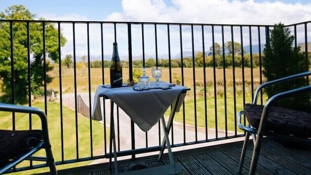 Un balcón con una mesa dispuesta para dos personas, con vistas a un paisaje cubierto de césped.