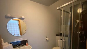 Un baño con lavamanos, espejo, inodoro y ducha con mampara de vidrio.