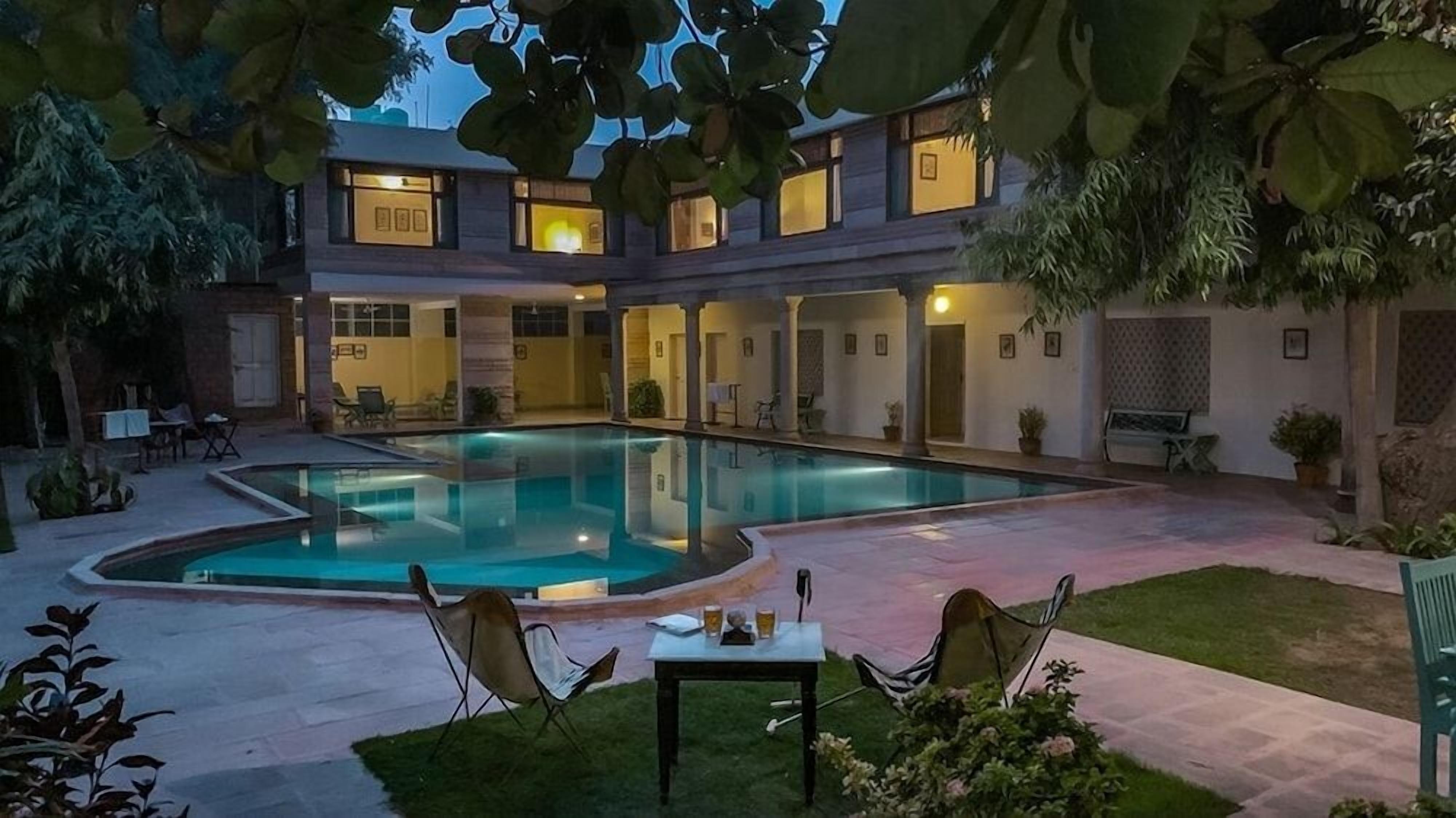 A pool area with a clear pool, surrounded by a patio with chairs and a table.