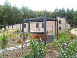 Ein moderner Außenbereich mit einem Holzbottich, einer Pergola und einem Gebäude mit großen Fenstern.