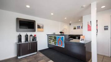 A reception area with a counter, a flat-screen TV mounted on the wall, a coffee machine, and a sign with the number 6.