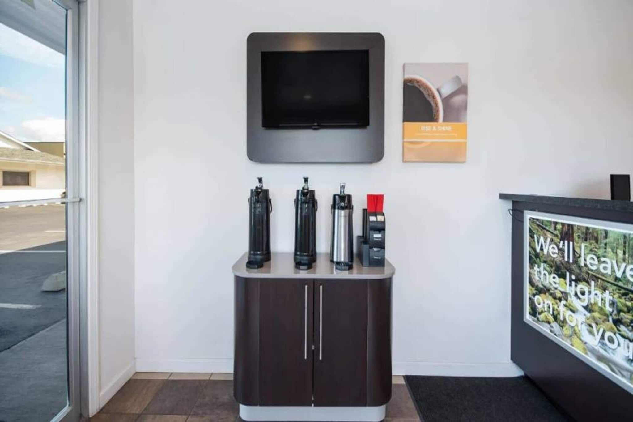 A reception area with a flat-screen TV mounted on the wall, a coffee machine, and a water dispenser on a counter.