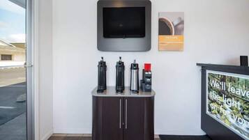 A reception area with a flat-screen TV mounted on the wall, a coffee machine, and a water dispenser on a counter.