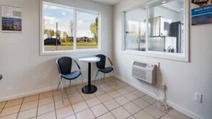 Una habitación con dos sillas, una mesita, una ventana que da a un estacionamiento y un aire acondicionado de pared.