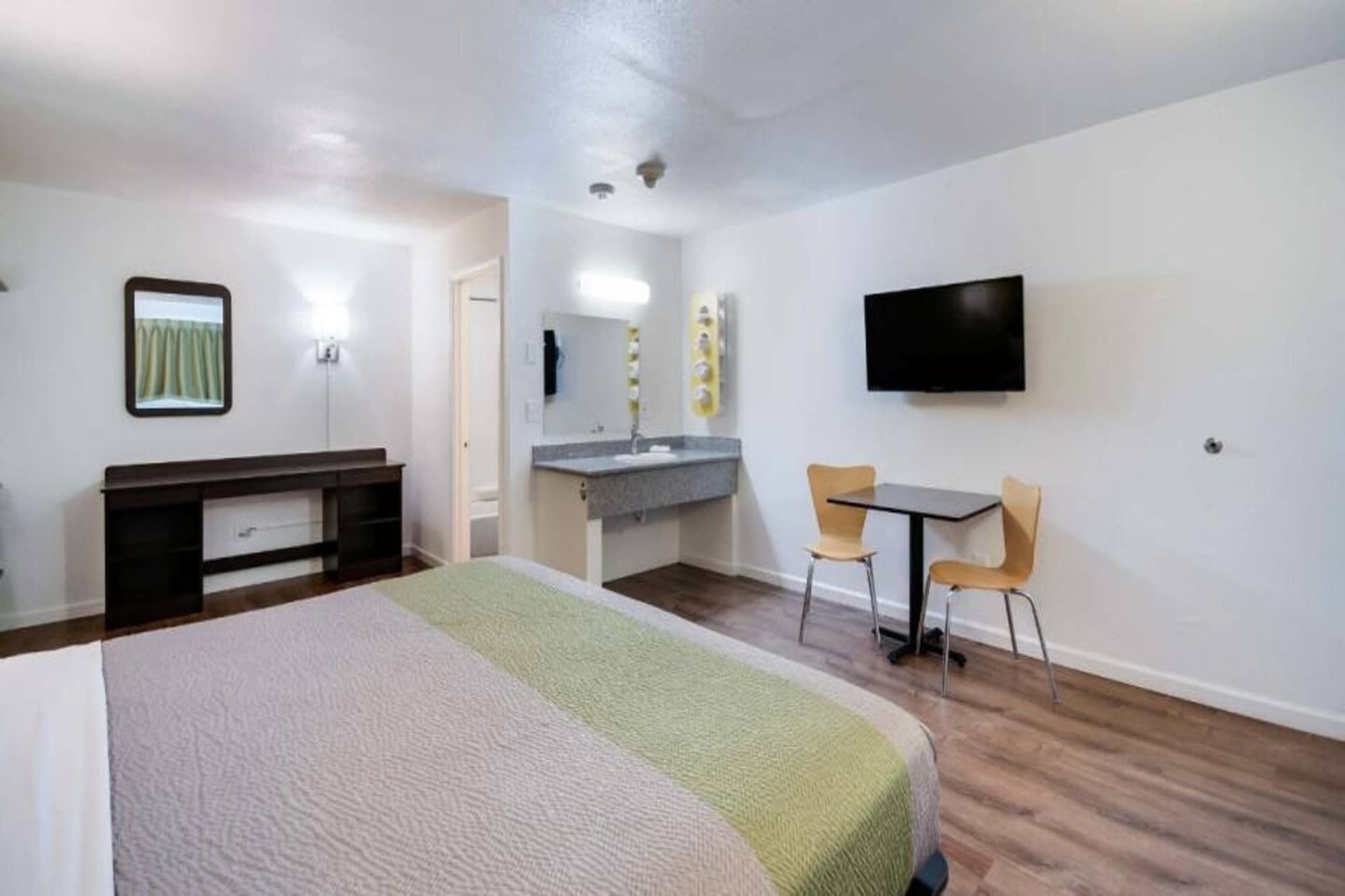 A hotel room with a bed, a desk with a chair, a television, and a bathroom with a mirror and sink.