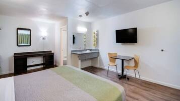 A hotel room with a bed, a desk with a chair, a television, and a bathroom with a mirror and sink.