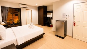 A hotel room with a bed, a desk, a chair, a TV, a refrigerator, and a door.