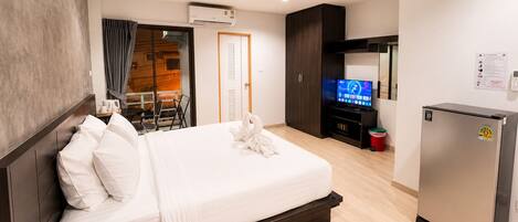 A hotel room with a bed, a television, a refrigerator, and a sliding door leading to a balcony.