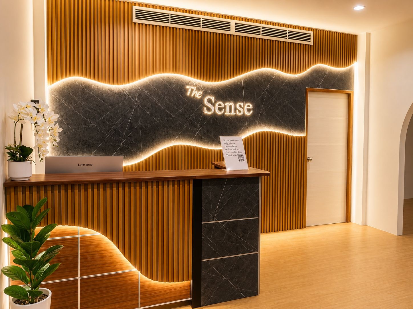 A reception desk with a Lenovo laptop, a sign reading 'The Sense,' and a plant.