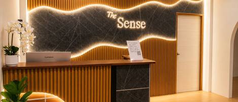 A reception desk with a Lenovo laptop, a sign reading 'The Sense,' and a plant.