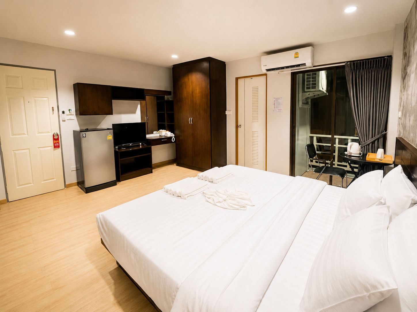 A hotel room with a bed, a desk, a refrigerator, a wardrobe, and a bathroom with a shower and toilet.