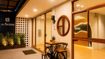 Entrada de un hotel con mostrador de recepción, puerta de cristal y un letrero que dice 'The Sense'.