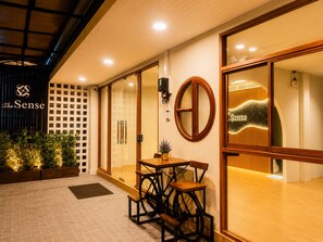 Entrada de un hotel con mostrador de recepción, puerta de cristal y un letrero que dice 'The Sense'.