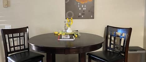 Una mesa redonda de comedor con dos sillas, un florero con flores amarillas y un libro sobre la mesa.