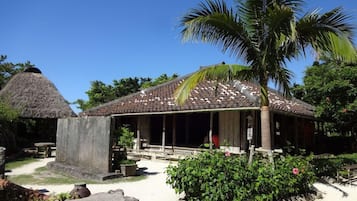 A traditional building with a tiled roof, a thatched structure, and a well-maintained garden with a palm tree.