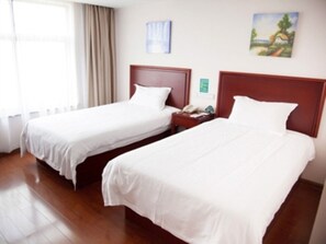 A hotel room with two single beds, wooden headboards, white bedding, a nightstand with a telephone, and a window with curtains.