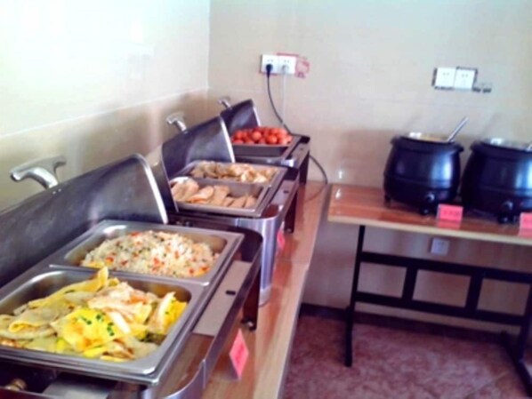 A buffet with various food options, a table with kettles, and a wall outlet.