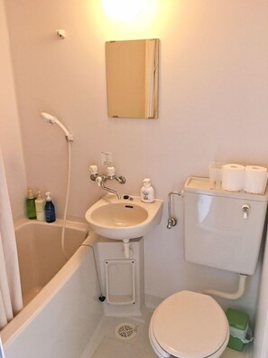 A small bathroom with a bathtub, sink, toilet, and a mirror. - Pension Coco (Ishigaki)