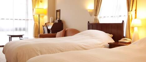 A hotel room with two beds, a desk, a chair, a lamp, and a window with curtains.