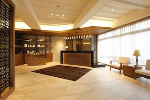 A modern lobby with a reception desk, seating area, and a decorative wall. - Provence (Shima)