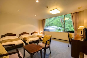 Une chambre d’hôtel avec deux lits, un bureau, une chaise et une grande fenêtre donnant sur les arbres.