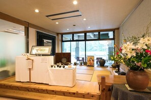 Una habitación tradicional japonesa con suelo de tatami, una disposición para ceremonia del té y un amplio ventanal que proporciona luz natural.