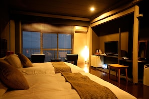Habitación de hotel con dos camas, un escritorio, televisor y ventana con persianas.