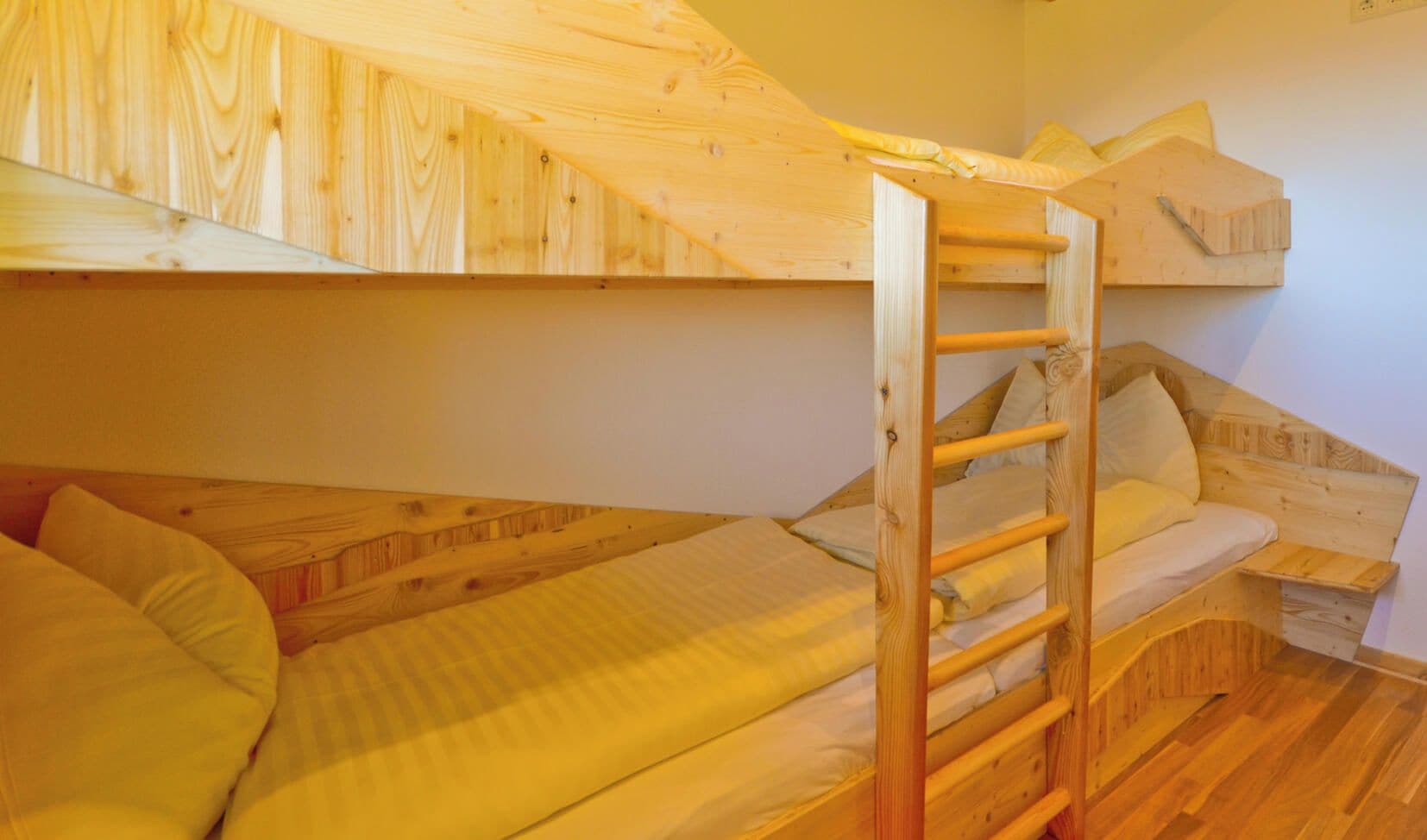 Une chambre avec un lit superposé, une petite échelle en bois, une étagère en bois et un plafond en pente.