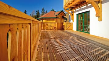 Eine Holzterrasse mit Schachbrettmuster, die zu einem Gebäude mit grüner Tür und Balkon führt.