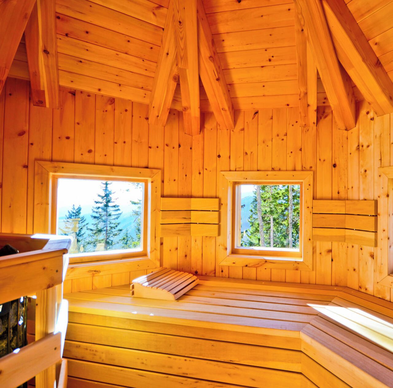 L’intérieur d’un chalet en bois, doté de deux fenêtres donnant sur des arbres et une montagne.