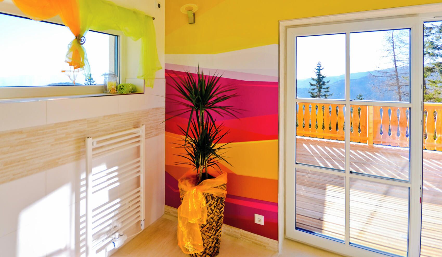 Quarto com radiador, planta em vaso, janela com vista para um terraço e parede colorida.