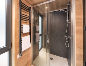 Eine moderne Dusche mit Glastür, einem Handtuchhalter mit mehreren Handtüchern und einer Wandverkleidung aus Holz.