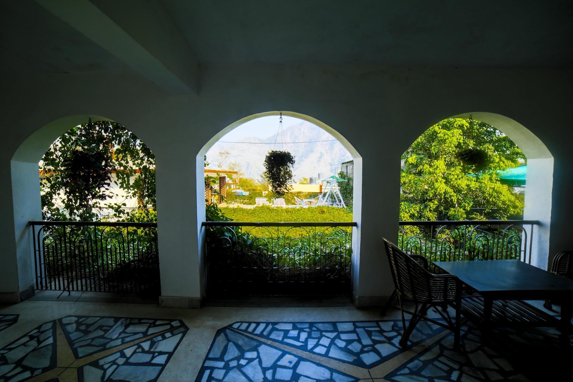 A covered outdoor area with a tiled floor, a table, chairs, and three arched windows overlooking a garden.