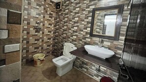 A bathroom with a tiled wall, a toilet, a sink, and a mirror. - Hotel Bom Sucesso (Candolim)