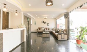 A hotel lobby with a reception desk, a sofa set, and a large window offering a view of the outdoors. - Treebo Sunrise (Chikkamagaluru)