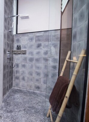Un área de ducha con pared de azulejos, un cabezal de ducha, un perchero para toallas y una escalera de bambú.