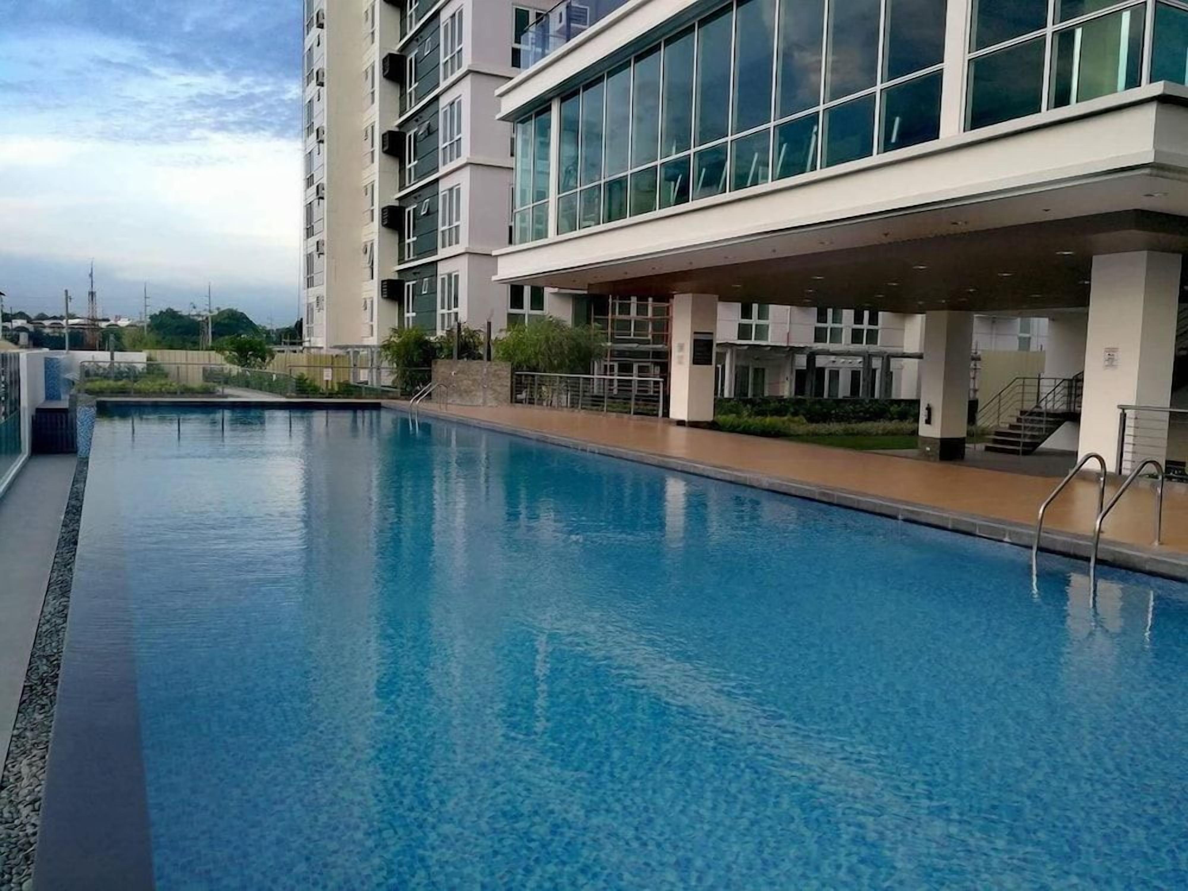 A swimming pool adjacent to a multi-story building with large windows and a covered walkway.