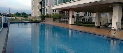 A swimming pool adjacent to a multi-story building with large windows and a covered walkway.